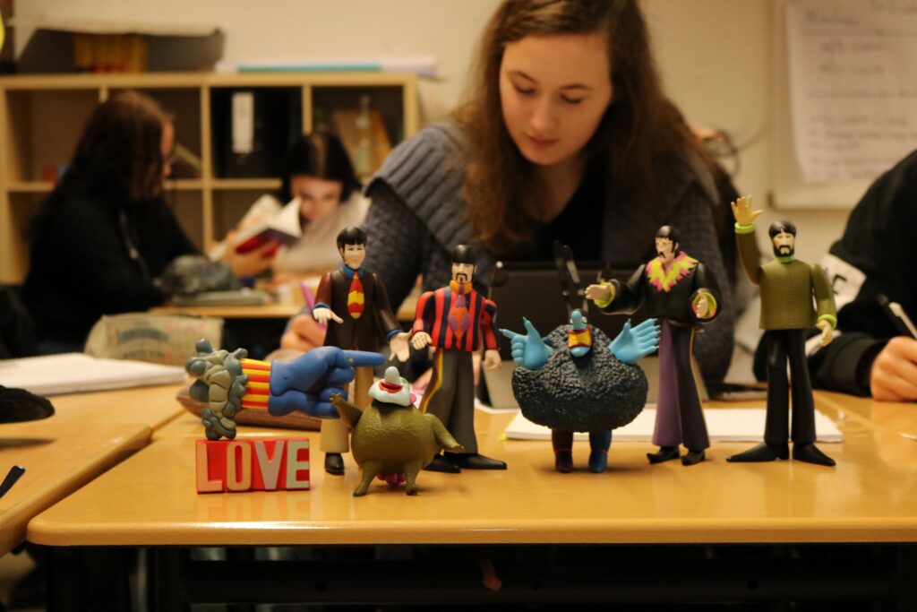 Verschiedene Figuren stehen auf einem Tisch, während Schüler im Hintergrund arbeiten.