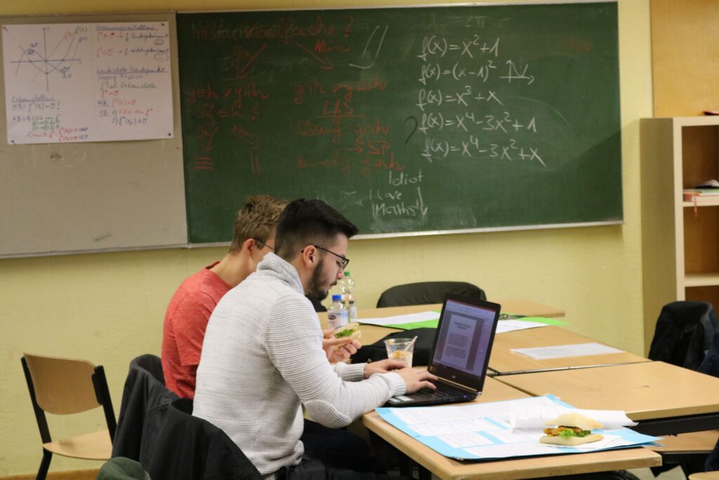 Schüler arbeiten am Laptop in einem Klassenraum mit grüner Tafel.