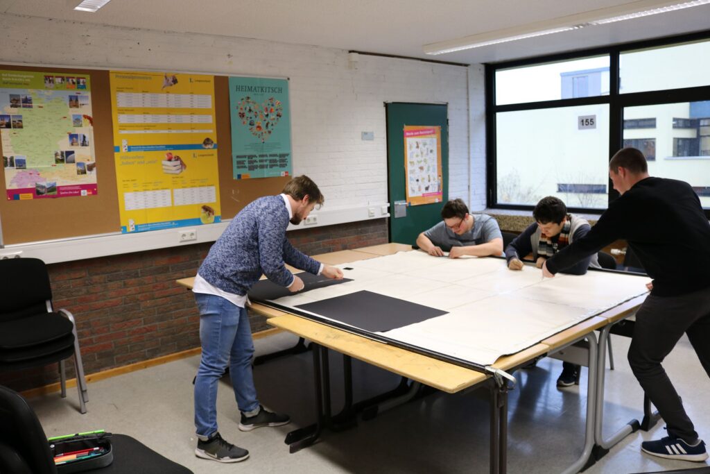 Schüler arbeiten an einem Tisch mit Papier und Materialien in einem Klassenraum.