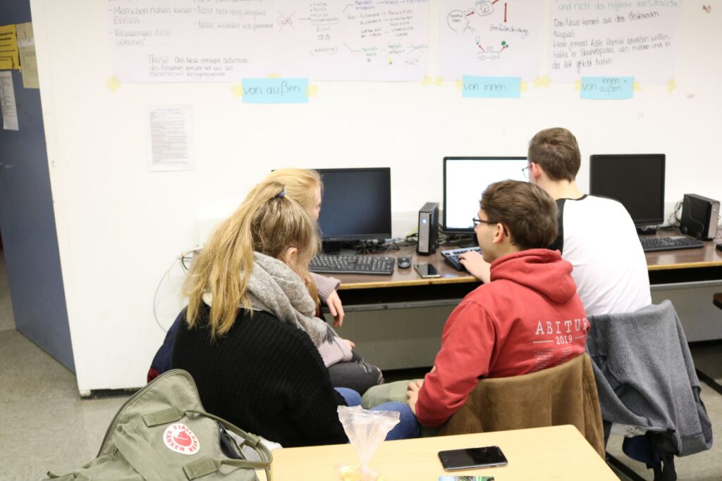 Vier Schüler sitzen an Computern und arbeiten zusammen an einem Tisch.
