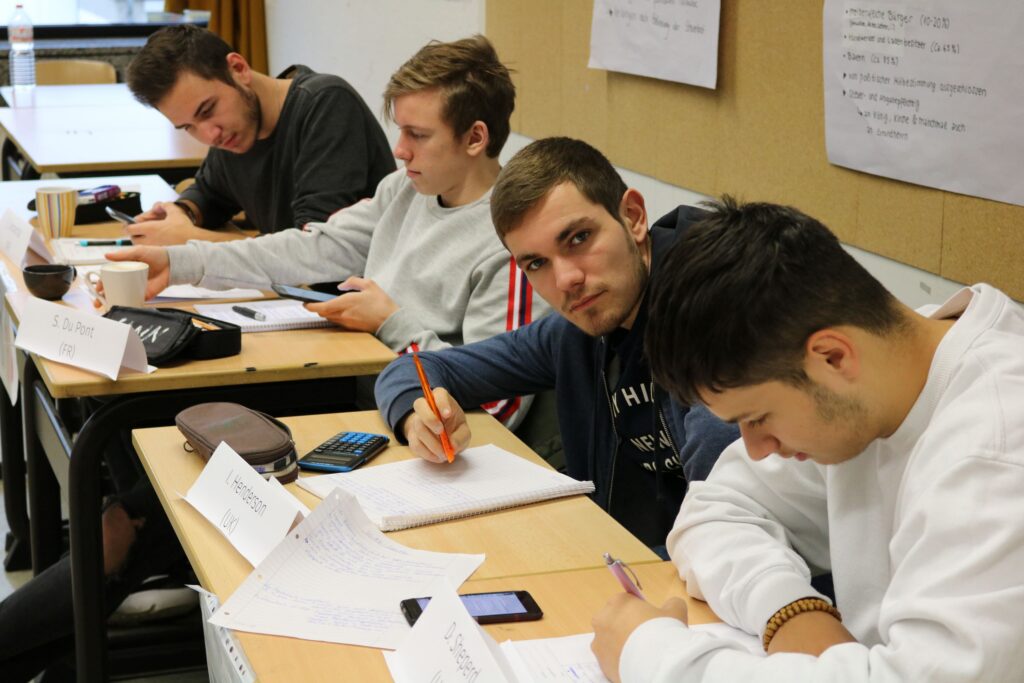 Vier Schüler sitzen an Tischen und schreiben in Notizhefte.