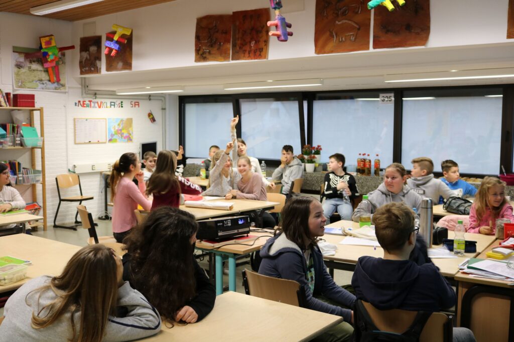 Schüler sitzen in einem Klassenraum und arbeiten an ihren Tischen.