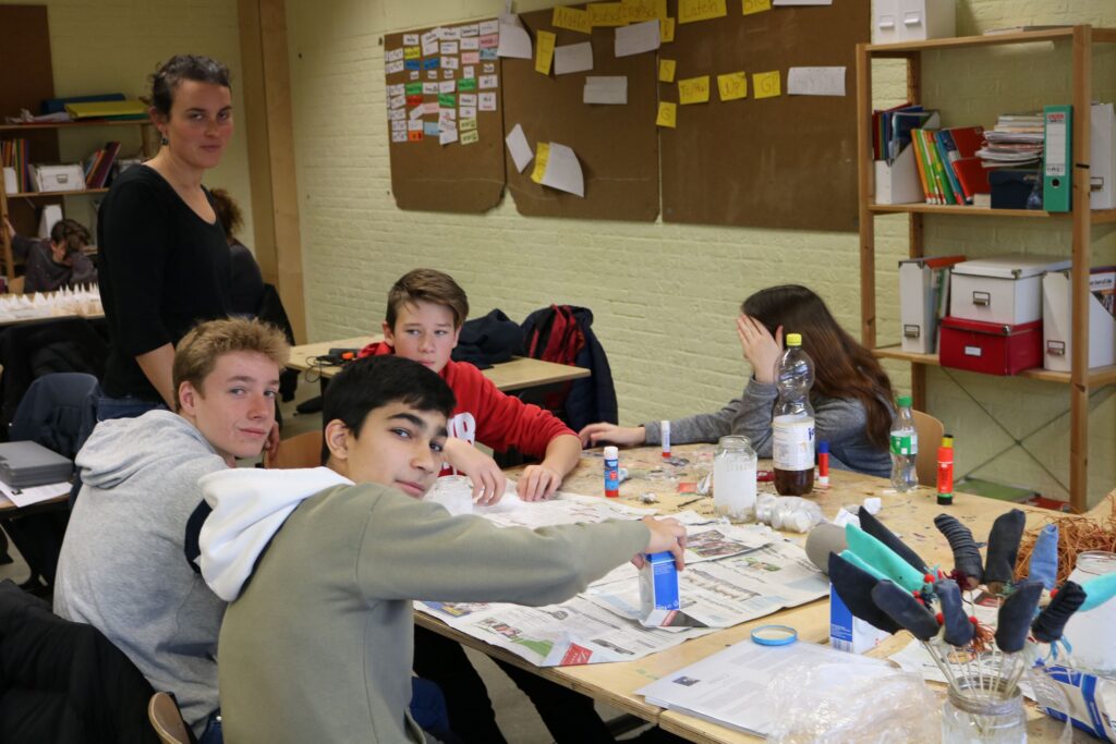 Schüler arbeiten an einem Tisch mit Bastelmaterialien in einem Klassenraum.