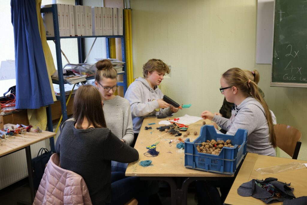 Schüler arbeiten an Bastelprojekten an einem Tisch in einem Klassenraum.