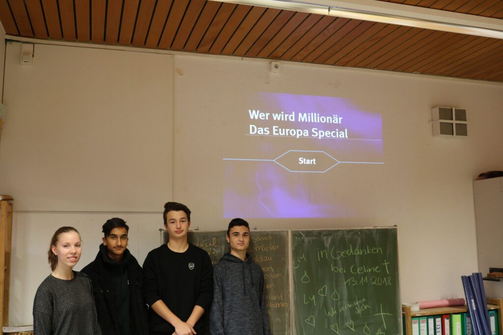 Gruppe von vier Schülern vor einer Wand mit Präsentation.