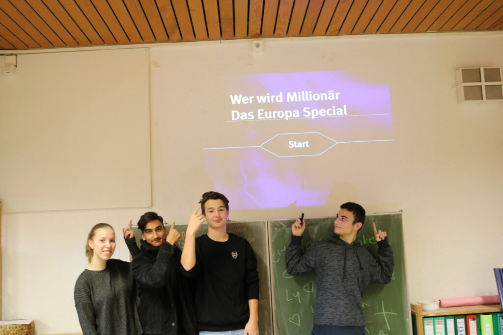 Vier Schüler stehen vor einer Wand mit einer Präsentation.