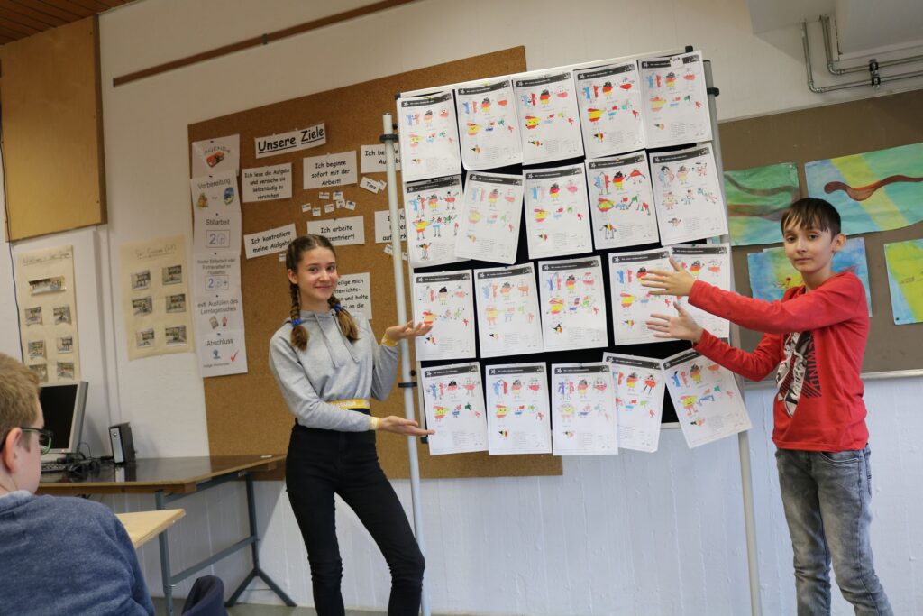 Schüler zeigen ihre Arbeiten an einem Präsentationsboard im Klassenraum.