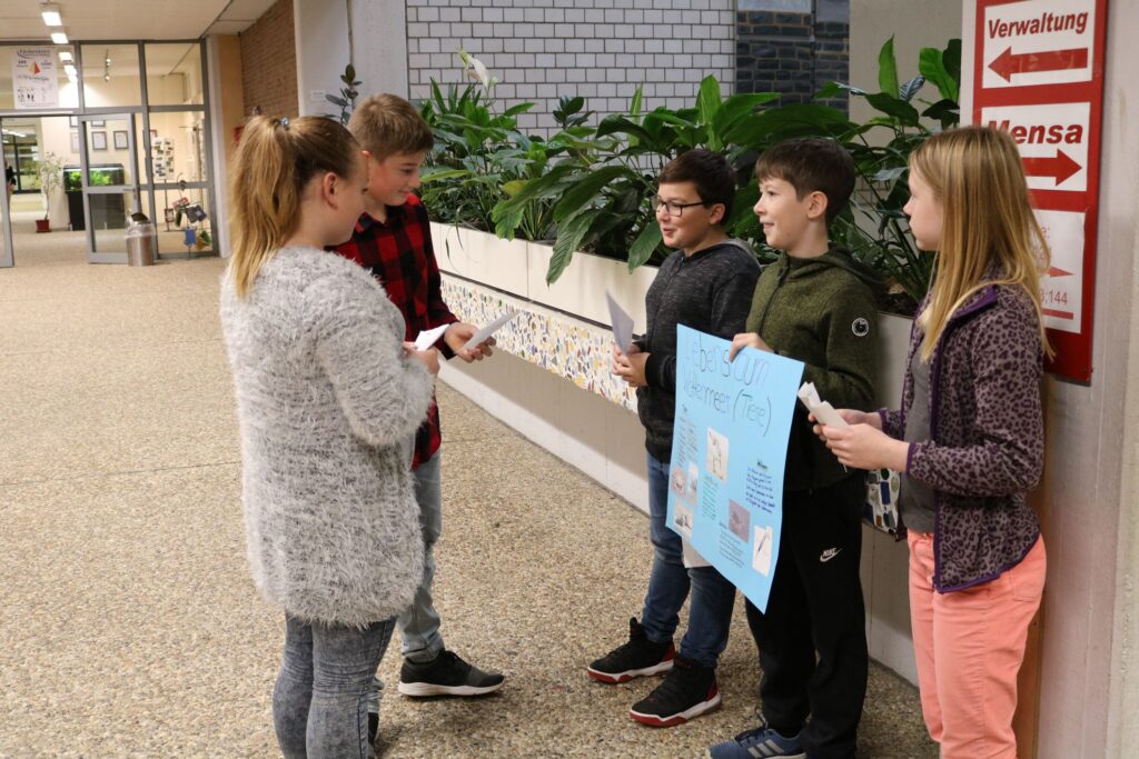 Schüler präsentieren ein Plakat in der Schulhalle.