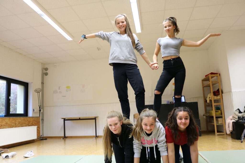 Fünf Mädchen bilden einen Menschenpyramide in einem Schulraum.