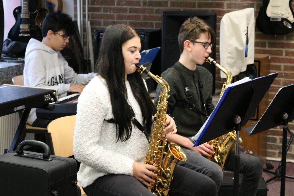 Schüler spielen Saxophon in einem Musikraum. Im Hintergrund ein Klavier.