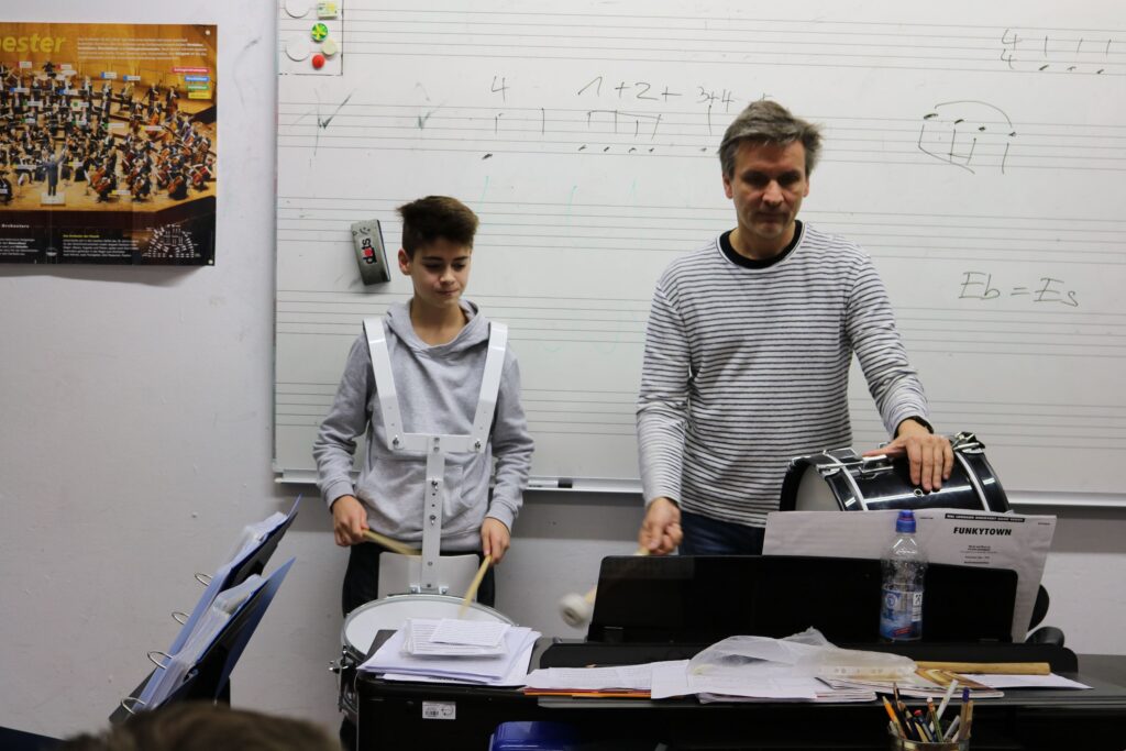 Ein Lehrer zeigt einem Schüler das Schlagzeugspiel im Musikunterricht.