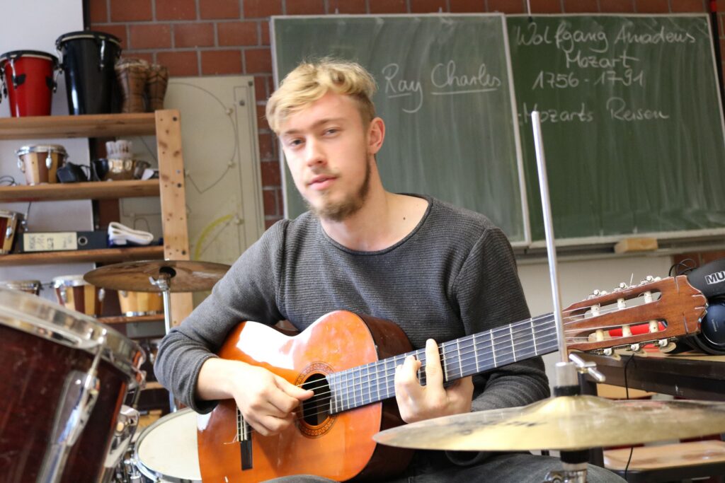 Ein junger Mann spielt Gitarre in einem Musikraum.