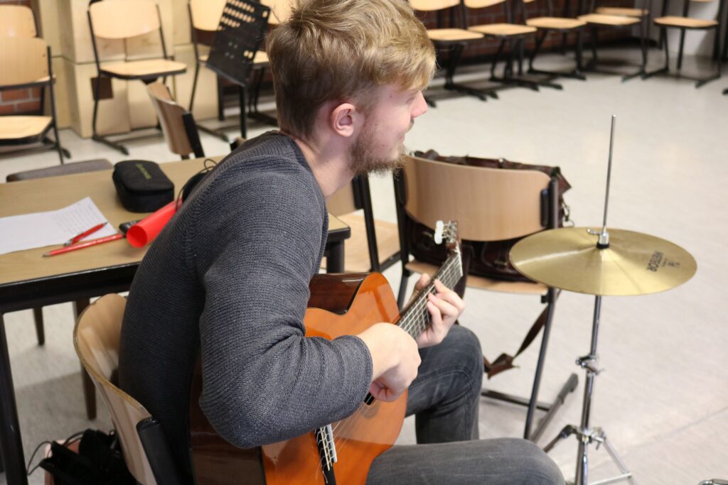Schüler spielt Gitarre in einem Klassenraum mit Musikinstrumenten.