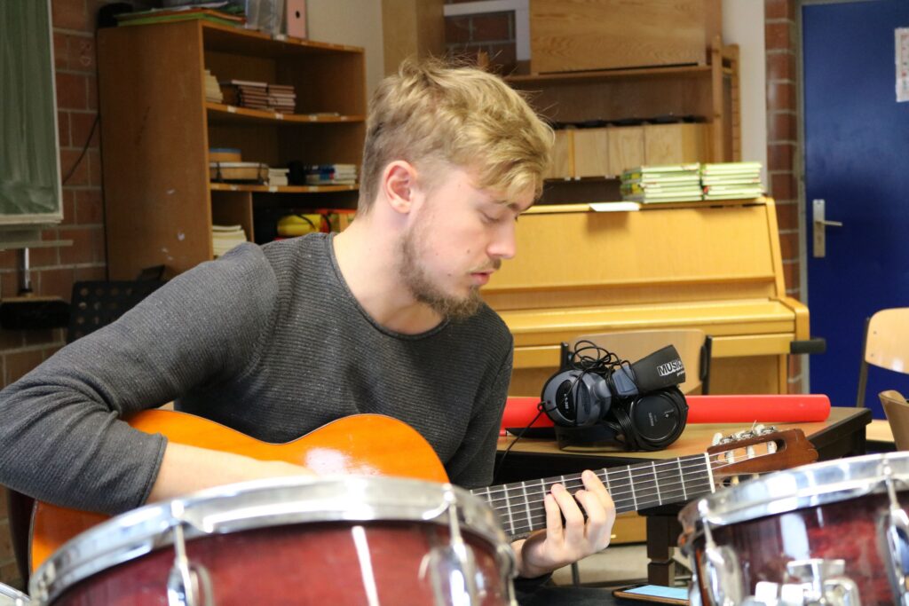 Junger Mann spielt Gitarre in einem Klassenzimmer.