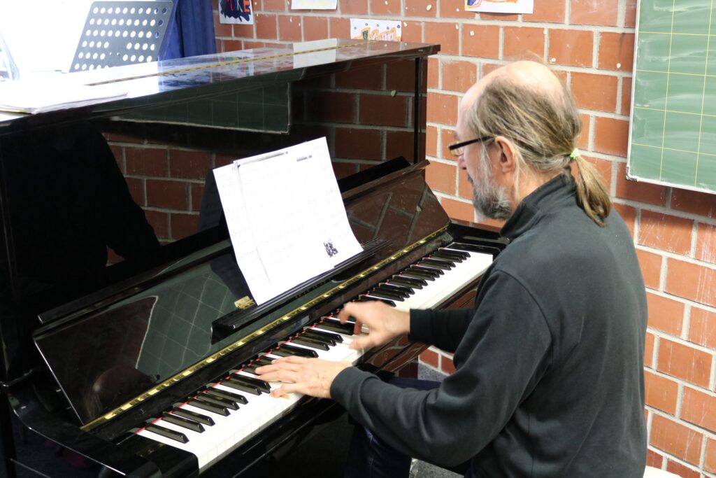 Ein Mann spielt Klavier und liest von einem Notenblatt ab.