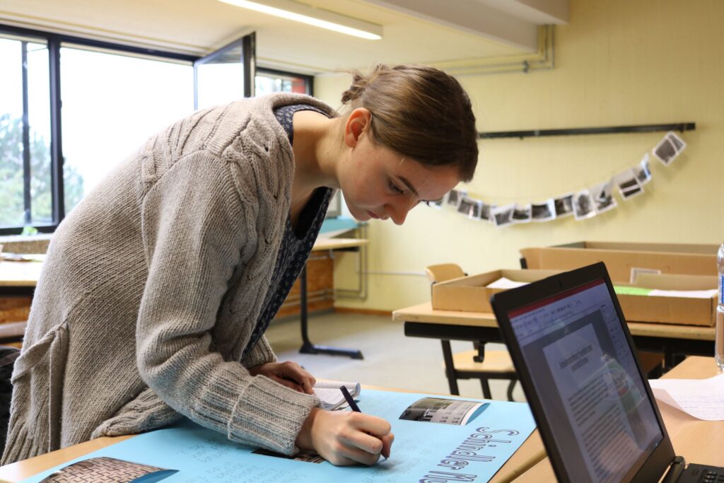 Schülerin schreibt an einem großen Blatt Papier in einem Klassenraum.