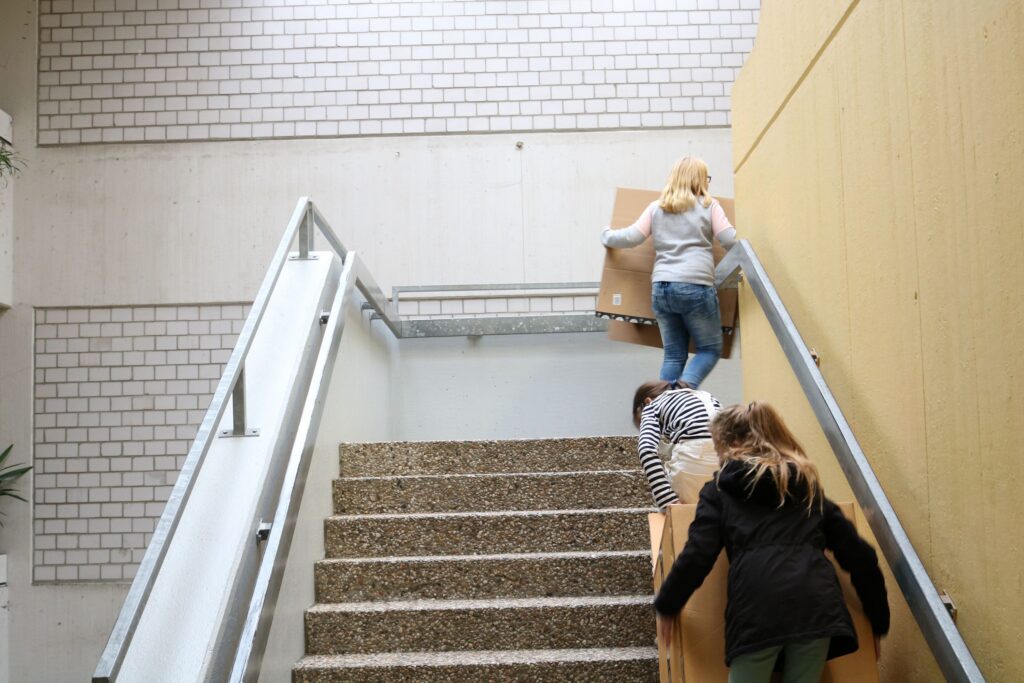 Schüler tragen Kartons eine Treppe hoch.