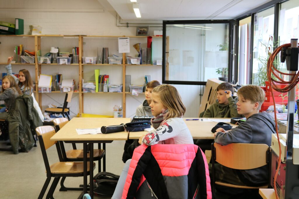 Schüler sitzen in einem modernen Klassenraum und hören aufmerksam zu.