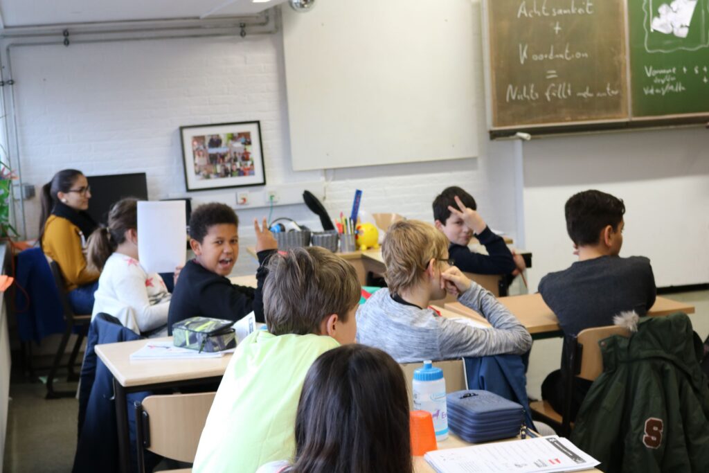 Schüler sitzen im Klassenzimmer, einige wenden sich zur Lehrerin um.