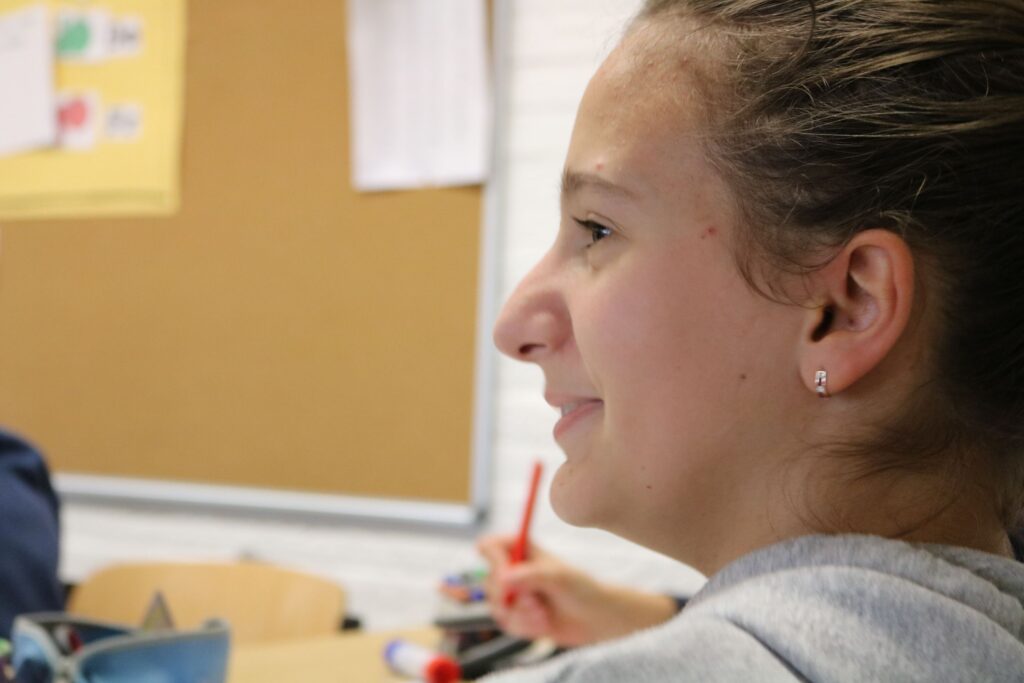 Schülerin in einem Klassenzimmer schaut nachdenklich zur Seite.