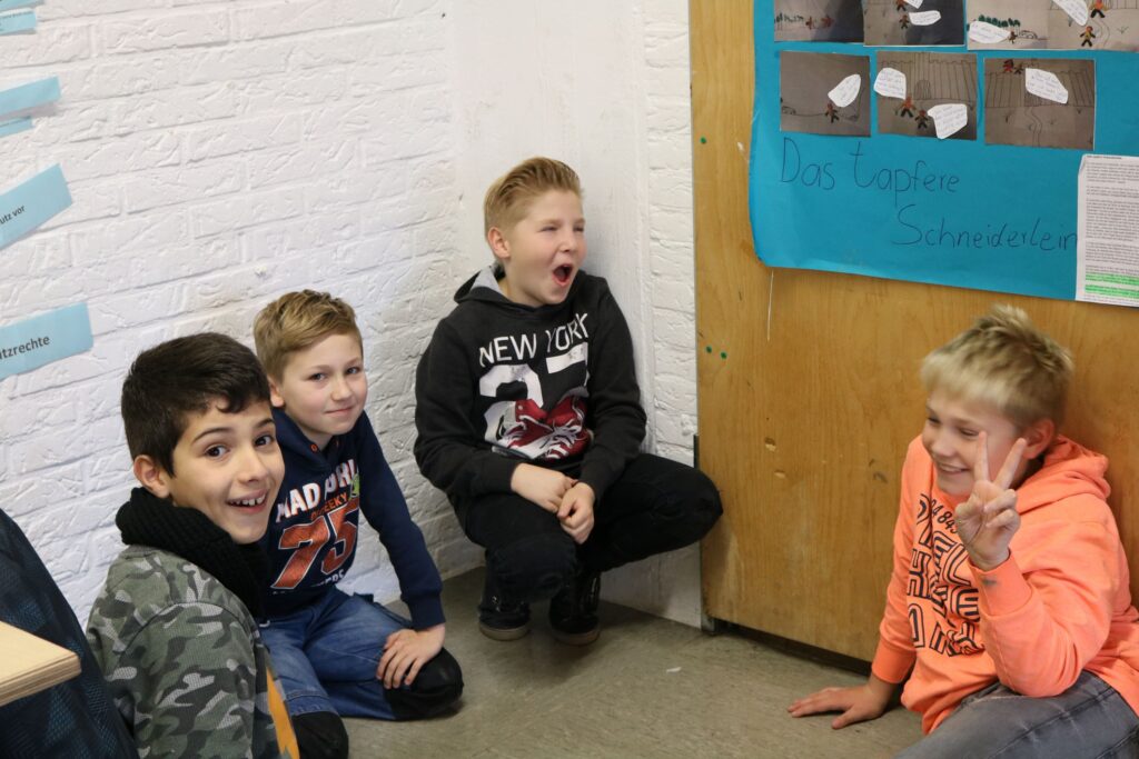 Vier Kinder sitzen im Klassenraum und lachen. Einer gähnt.