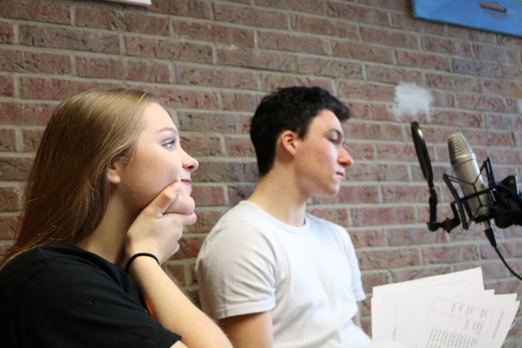 Schüler sitzen vor einem Mikrofon und bereiten sich auf eine Aufnahme vor.