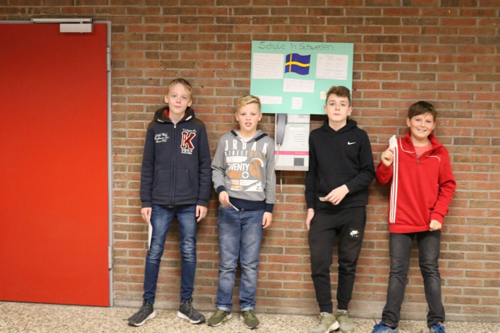 Vier Kinder stehen vor einer Backsteinmauer neben einer Informationstafel.