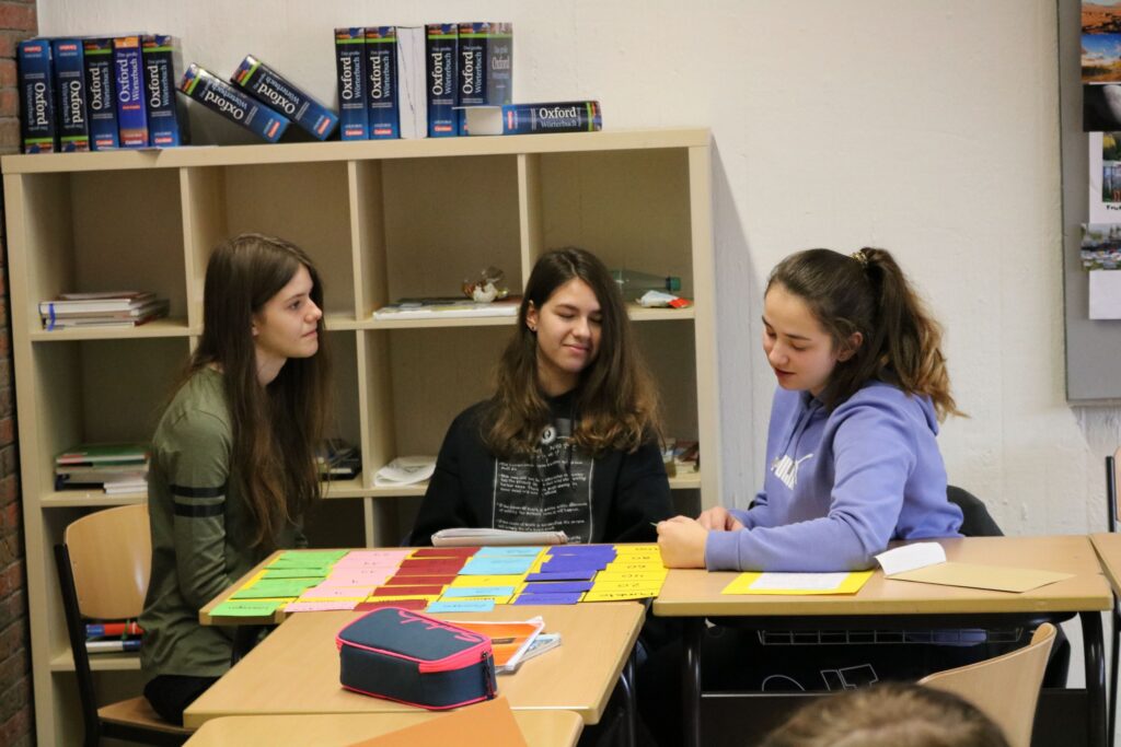 Drei Schülerinnen arbeiten gemeinsam an einem Tisch mit Lernmaterialien.