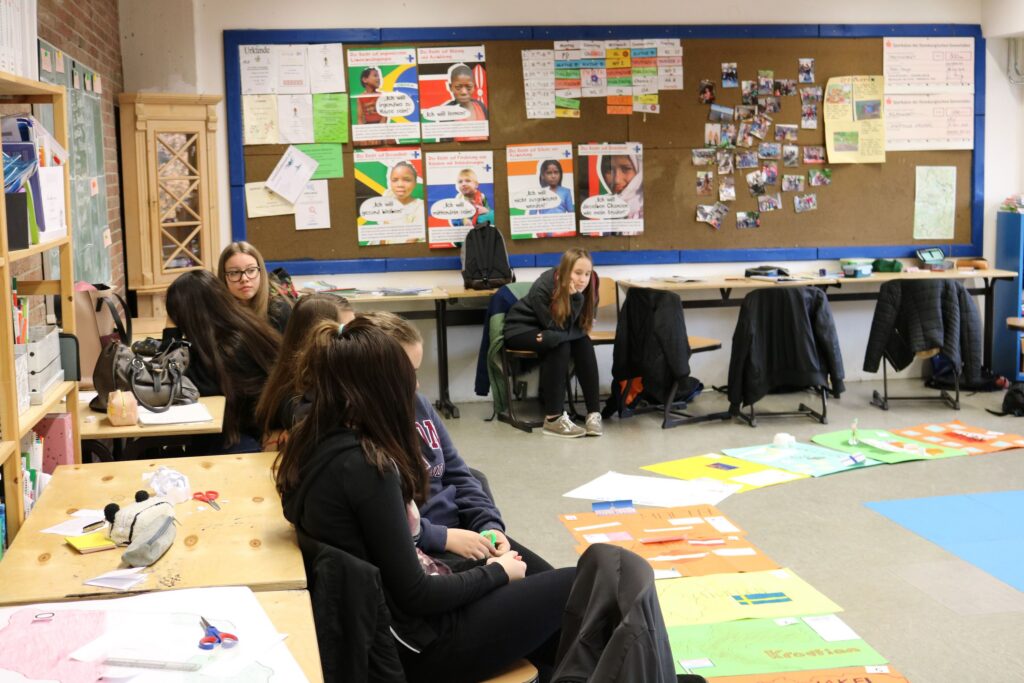Schülerinnen sitzen in einem Klassenraum mit Plakaten und Arbeitsmaterialien.