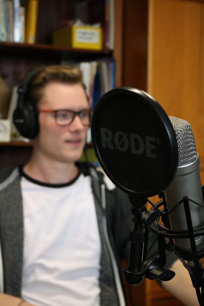 Junger Mann mit Kopfhörern sitzt vor einem Mikrofon.