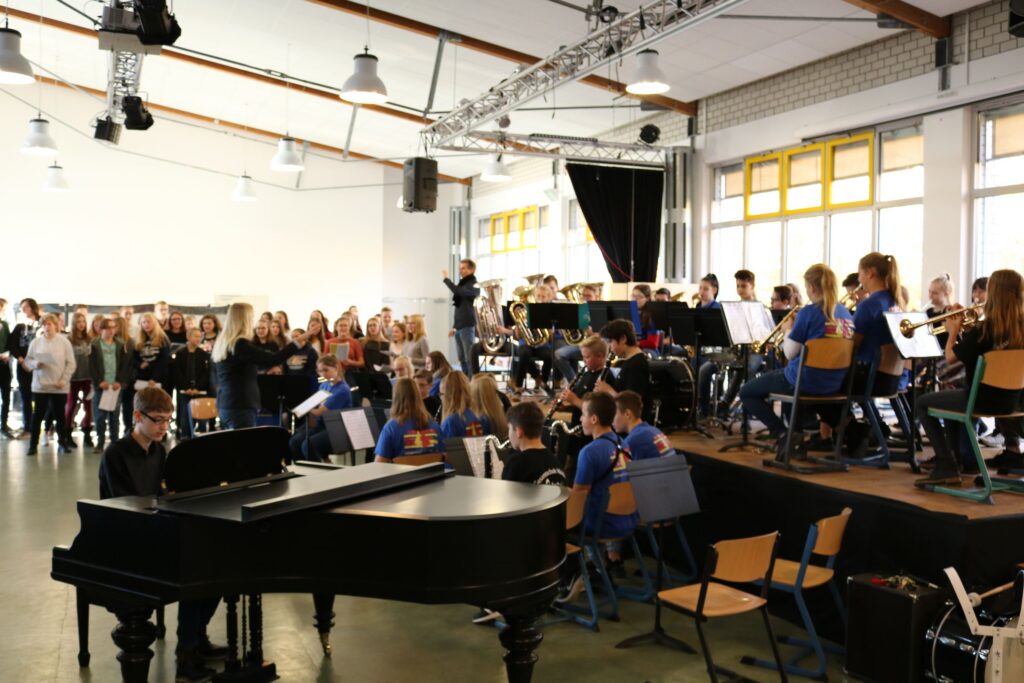 SchülerInnen spielen in der Aula ein Konzert, Publikum sitzt auf Stühlen.