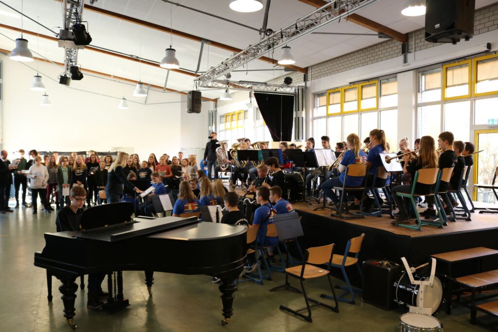 Schüler bei einem Musikauftritt in einer Aula mit Publikum und verschiedenen Instrumenten.