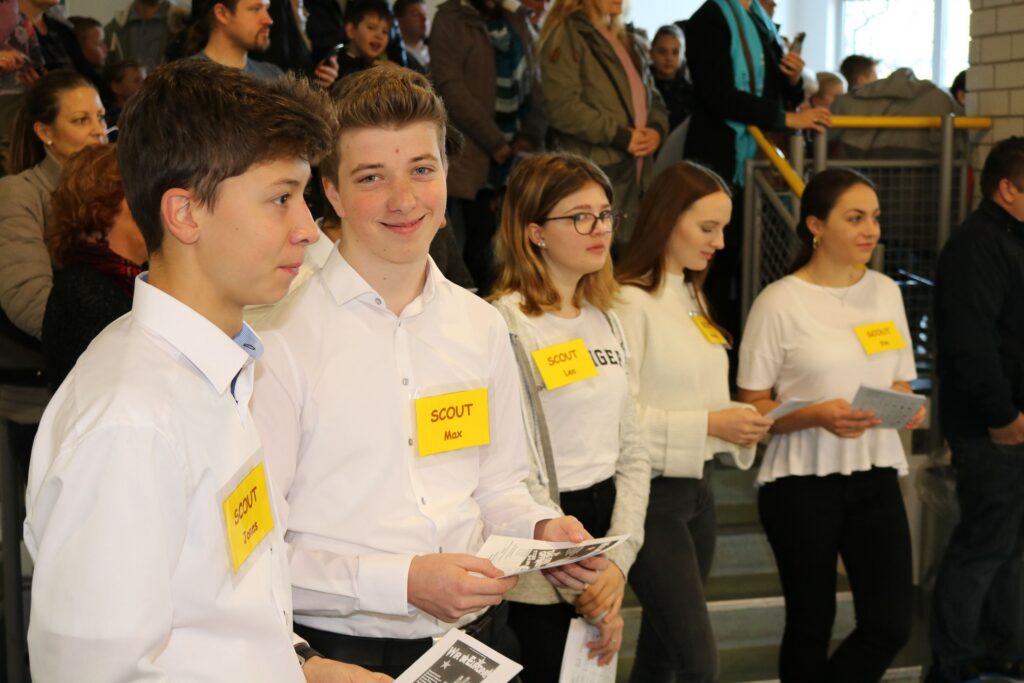 Schüler in weißen Hemden stehen mit Handzetteln in einer Menschenmenge.