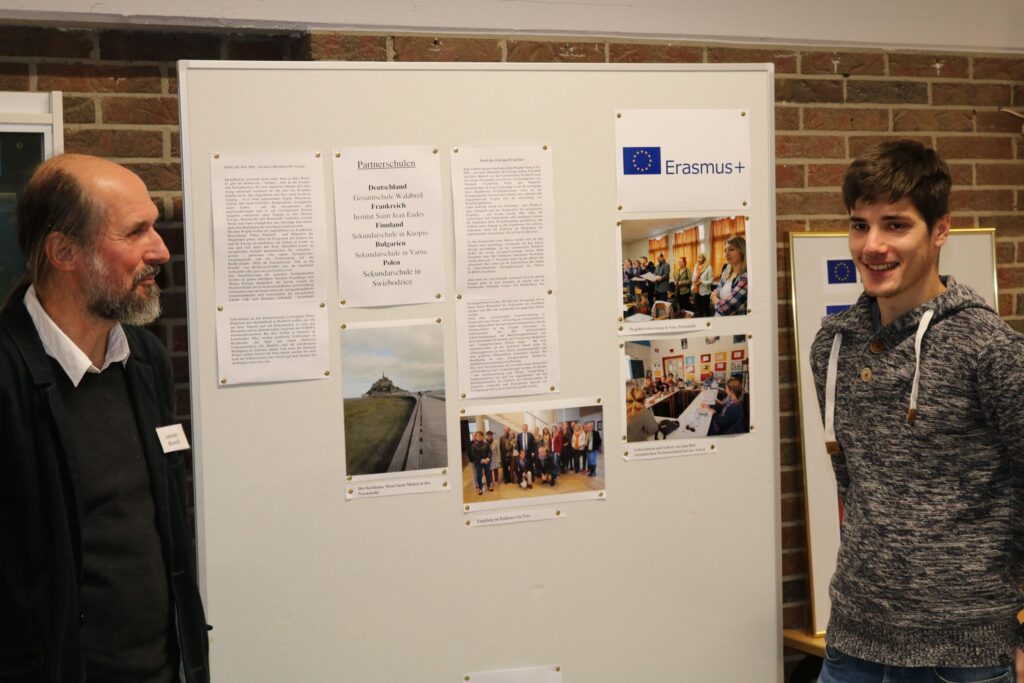 Zwei Personen stehen neben einer Präsentation über Erasmus+.