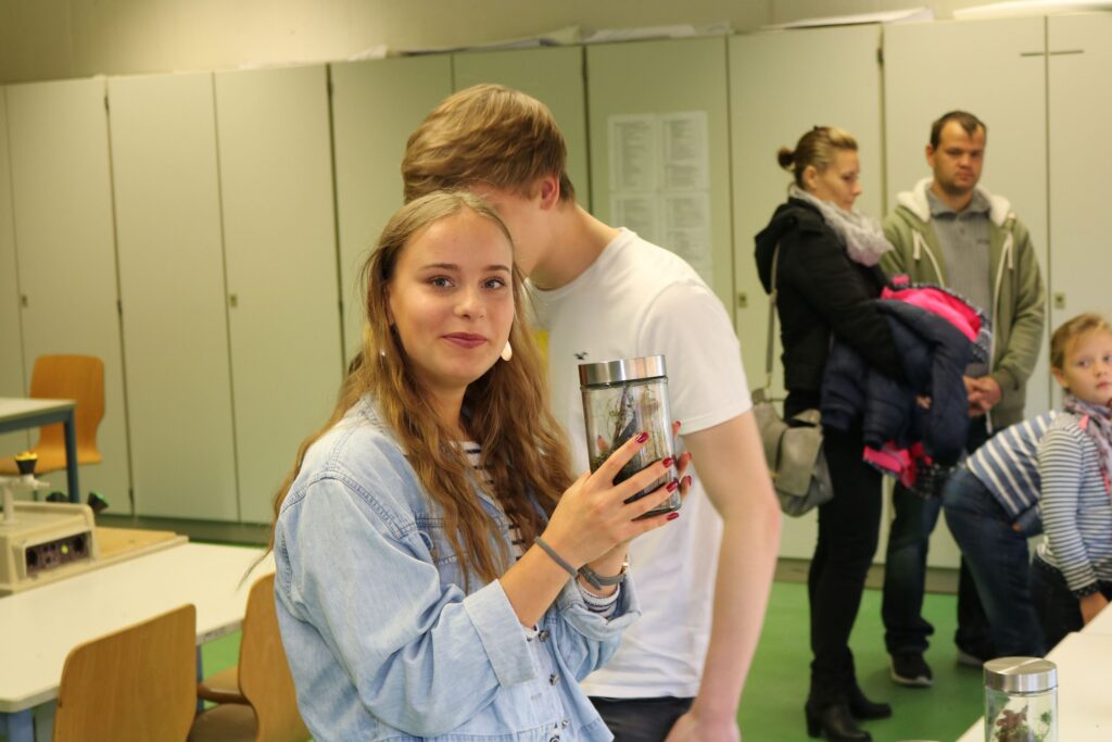 Eine Schülerin hält einen Becher in der Hand, andere Personen im Hintergrund.
