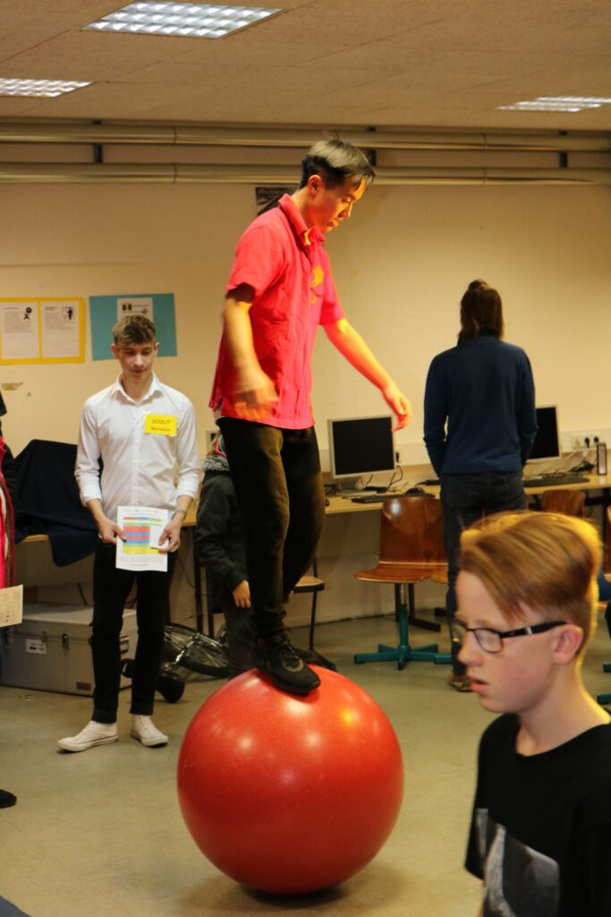Schüler balanciert auf einem großen Ball in einem Klassenraum.