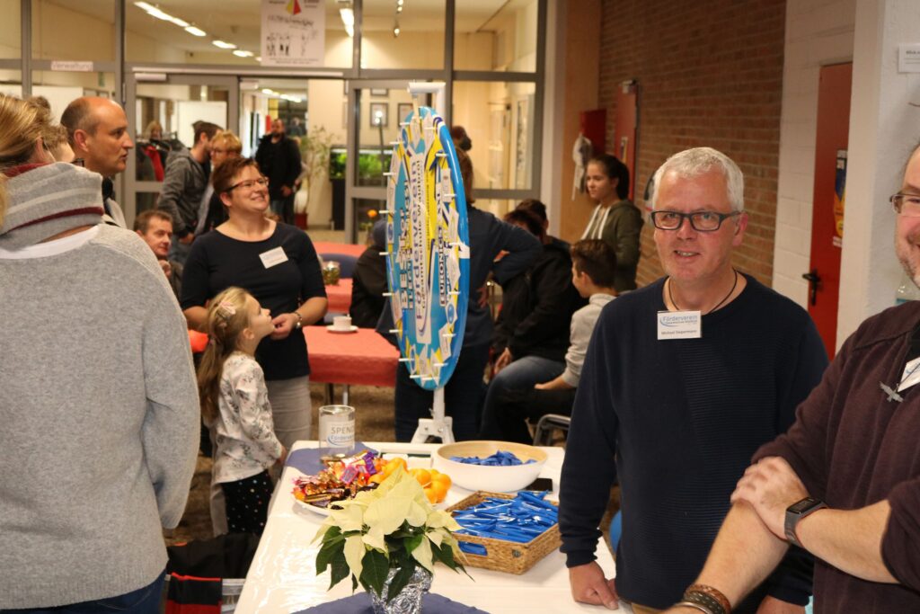 Menschen stehen an einem Tisch mit Snacks und Informationsmaterial in einer Schulumgebung.
