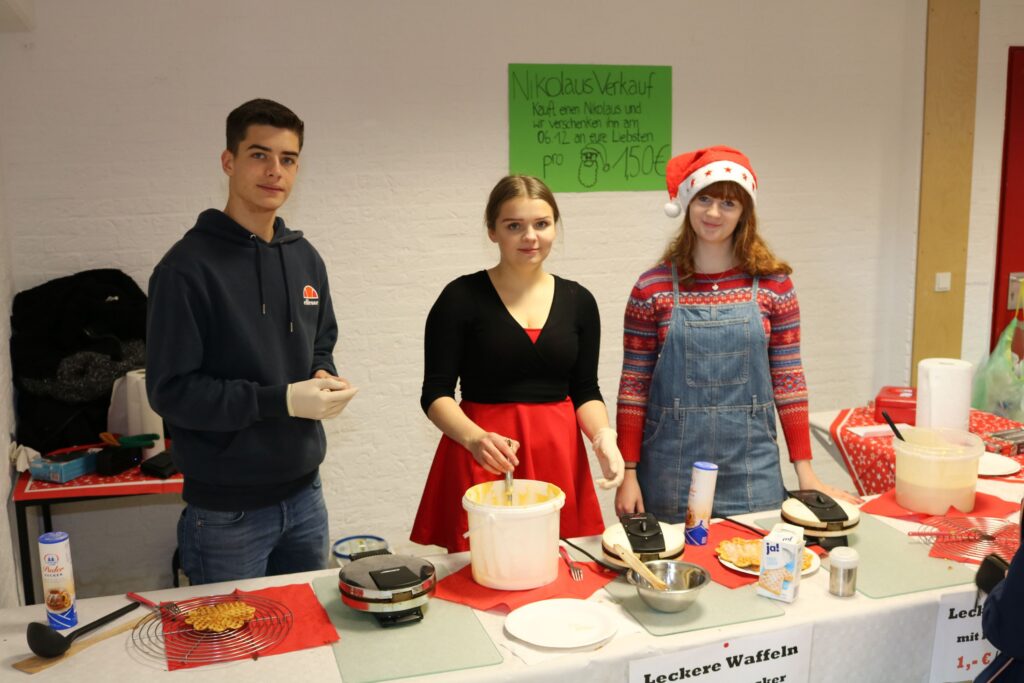 Drei Schülerinnen stehen an einem Tisch mit Essensangeboten.