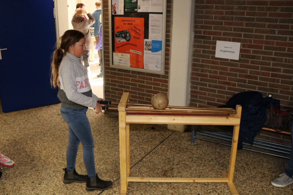 Ein Mädchen steht vor einem Holztisch mit einem Ball und einem Spielgerät im Flur.