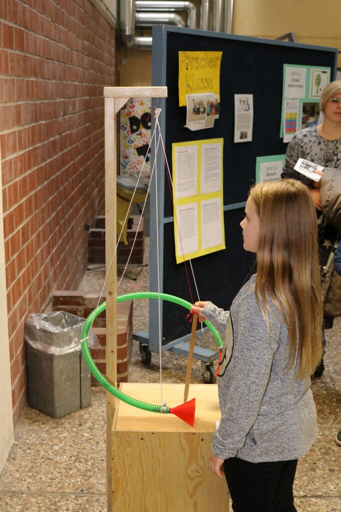 Mädchen mit langen Haaren betätigt eine physikalische Experimentieranlage in der Schule.
