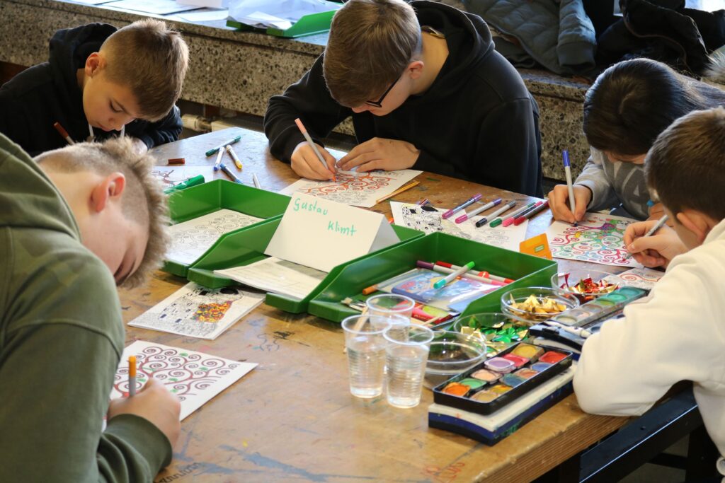 Schüler färben und zeichnen an einem Tisch mit verschiedenen Materialien.