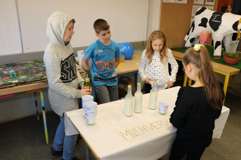 Kinder stehen an einem Tisch und füllen Flaschen mit Flüssigkeit.