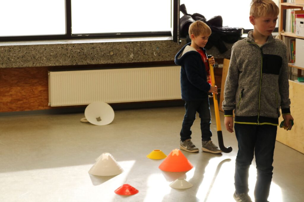 Zwei Kinder in einem Raum mit Übungsmarkierungen auf dem Boden.