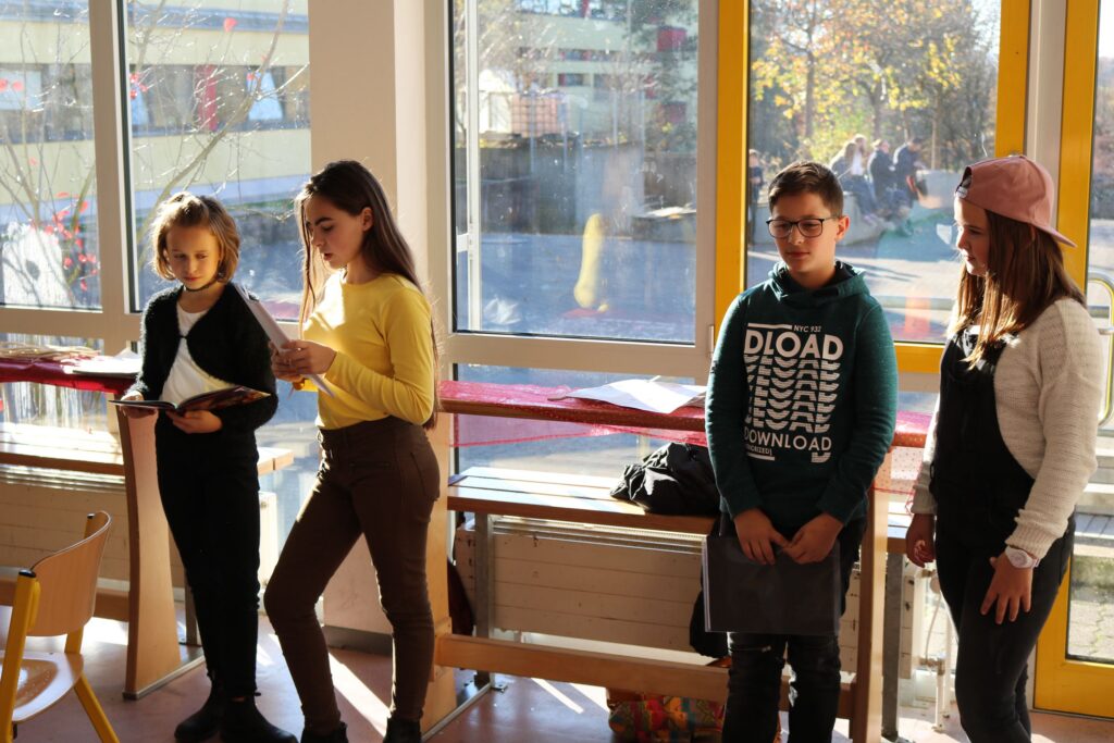 Vier Schülerinnen und Schüler stehen im Klassenzimmer und sprechen miteinander.