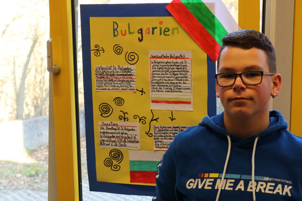Schüler steht vor einem Plakat über Bulgarien, das Informationen und Illustrationen zeigt.