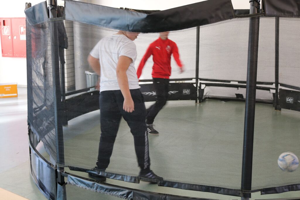 Zwei Personen spielen Fußball in einem Trainingsbereich mit Netz.