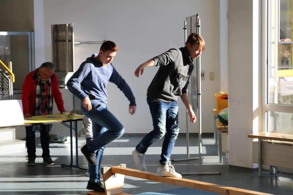 Zwei Schüler balancieren auf einer schrägen Fläche in einem Klassenraum.