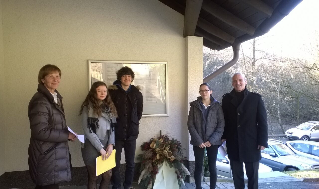 Gruppe von vier Personen steht vor einem Gebäude mit Blumenarrangement.