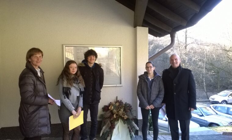 Gruppe von vier Personen steht vor einem Gebäude mit Blumenarrangement.