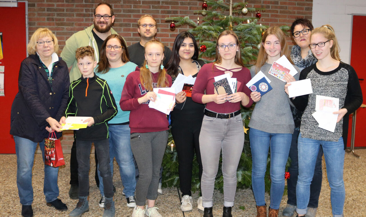 Gruppe von Schülern und Lehrern vor einem Weihnachtsbaum mit Auszeichnungen und Geschenken.